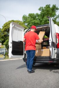 A Man in Red Shirt and Blue Denim Pants Standing beside White Van